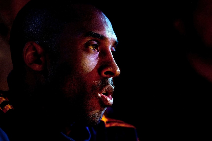 Kobe Bryant appears in shade with his mouth slightly open, looking off to the right of the picture