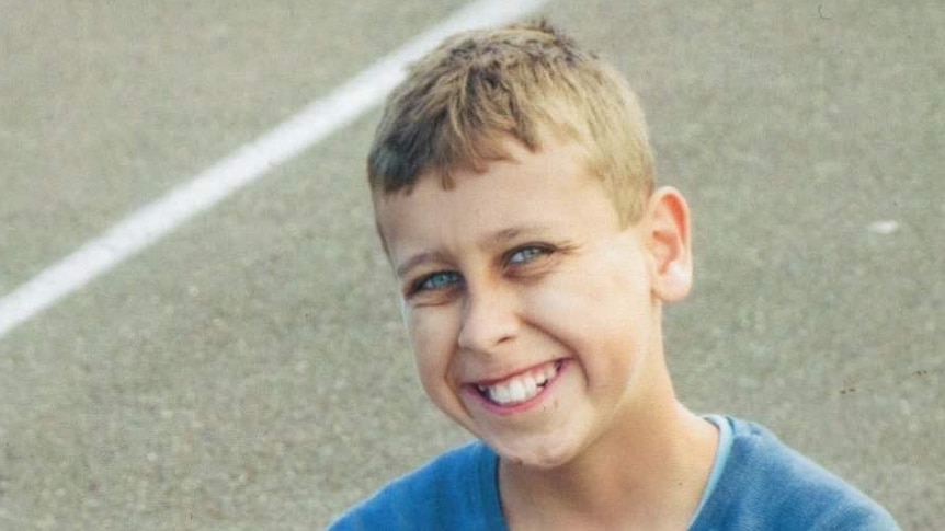 a young boy smiling while sitting on the ground