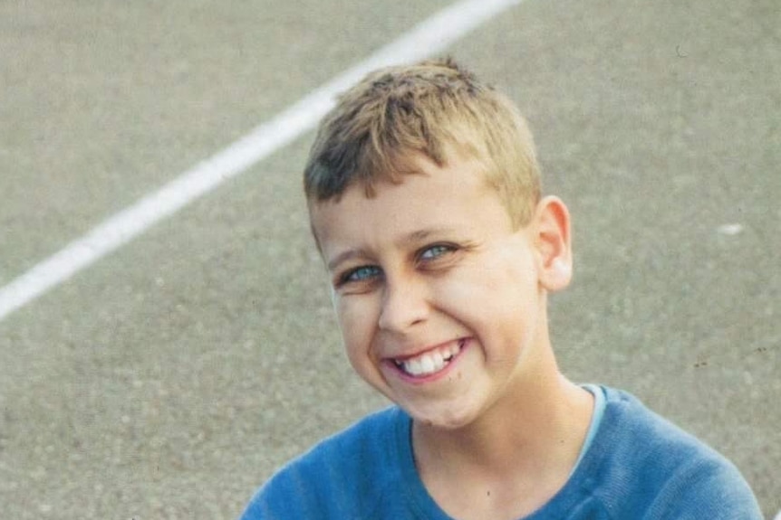 a young boy smiling while sitting on the ground