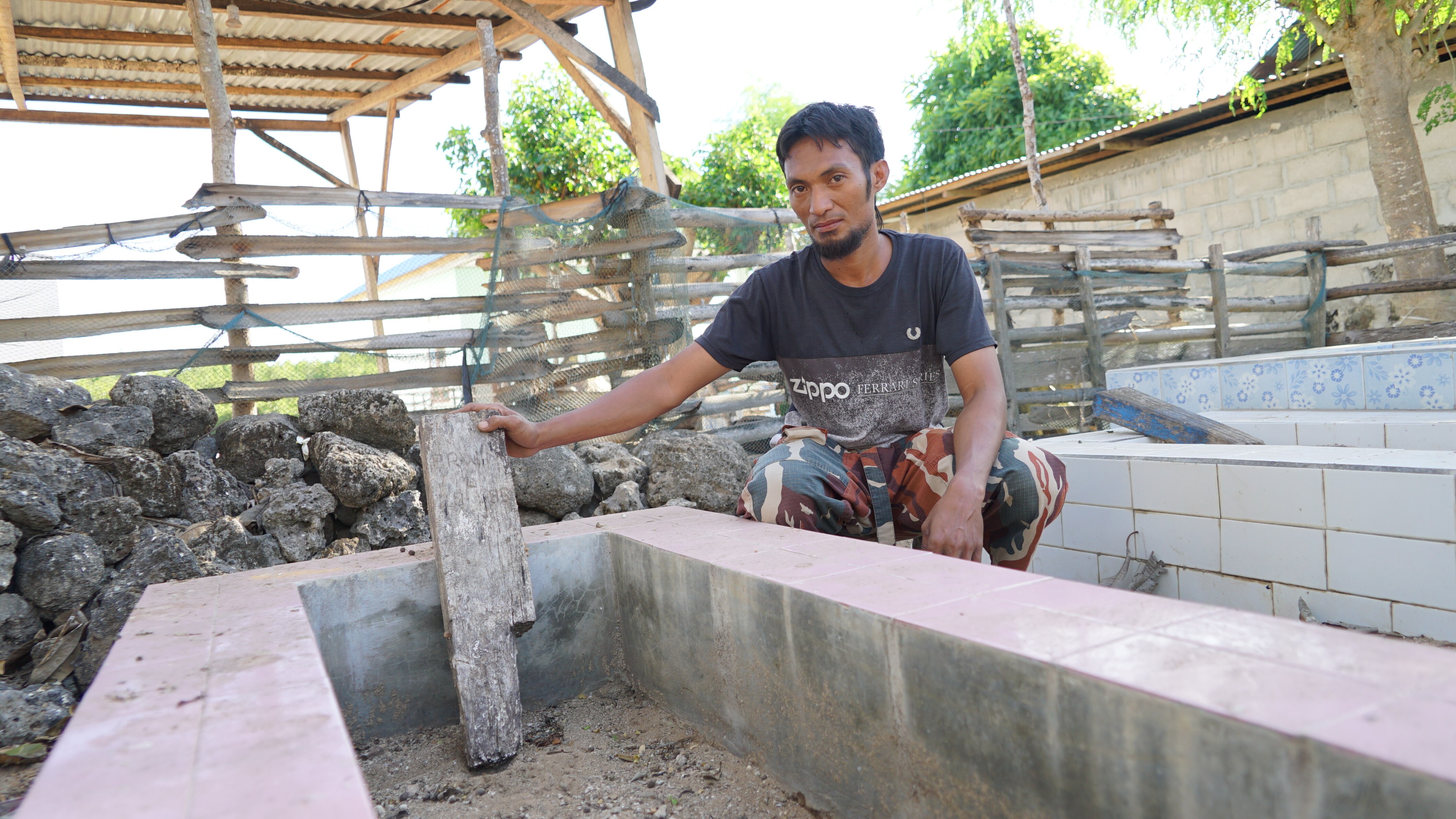 A man crouches down beside a cement grave site. 