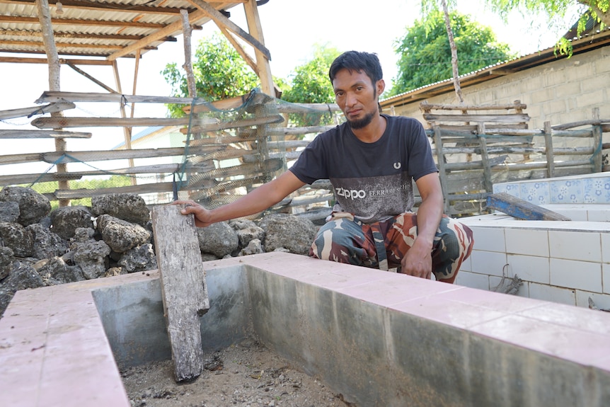 A man crouches down beside a cement grave site. 