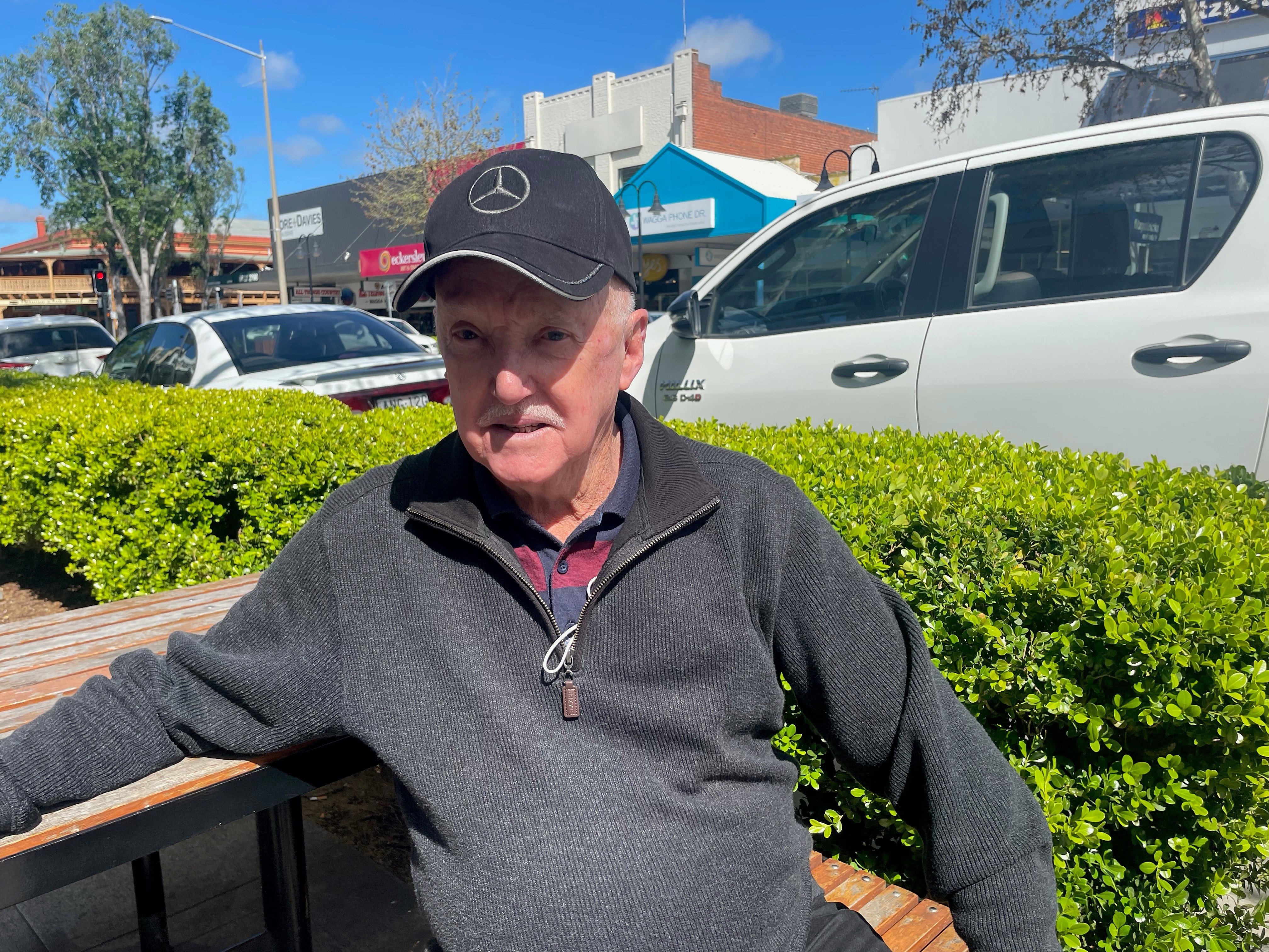Man in grey jumper and black cap, sitting on a park bench