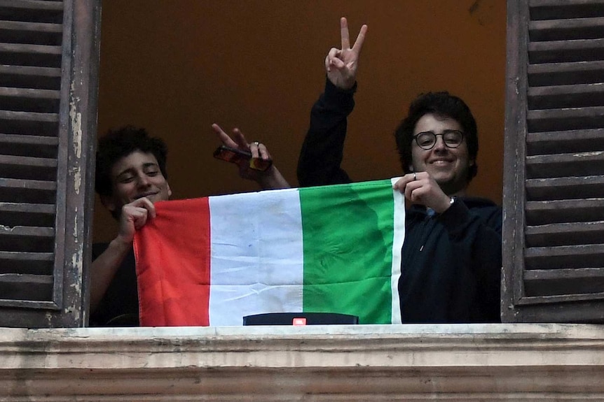 Two young Italians giving peace signs while holding up their flag