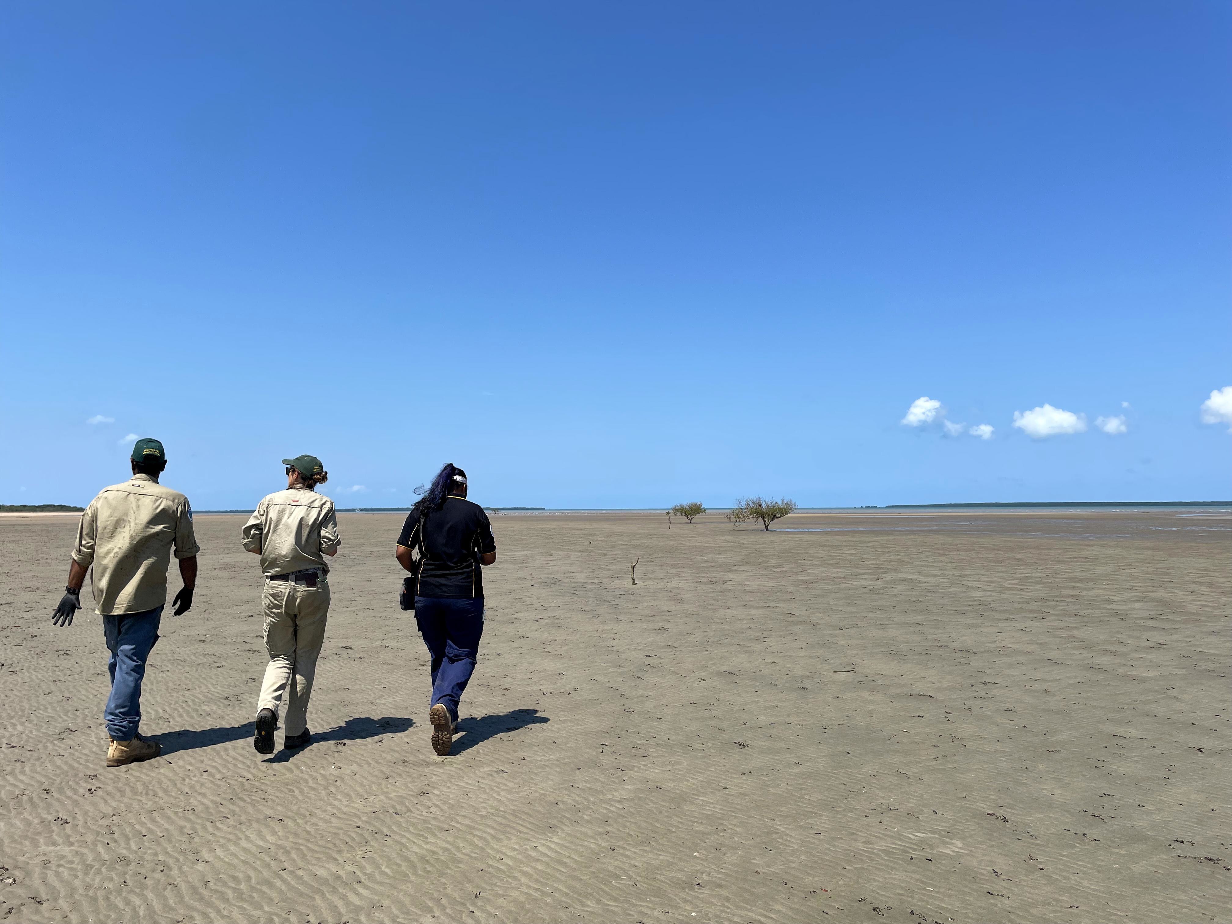 Three people walk across a beach on the Timor Sea