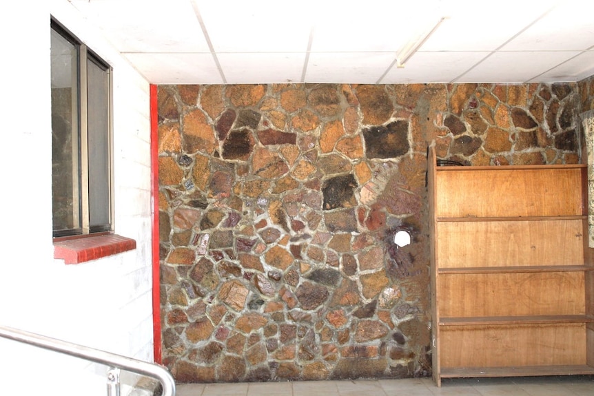 A rock wall and bookcase inside a home with red window sill.