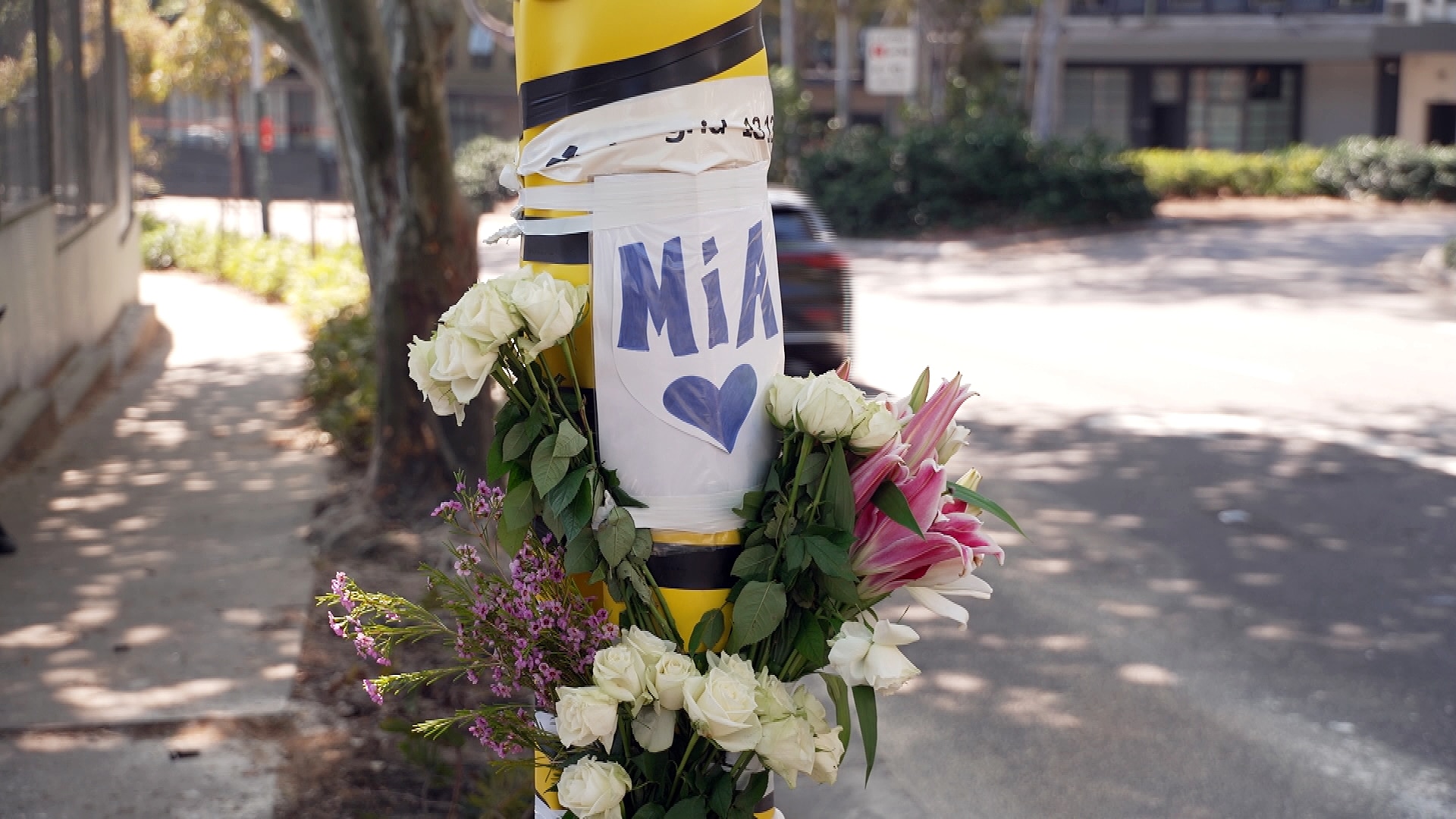 flowers with a sign that read mia on a pole at the site where a young police  officer died after the car crashed into a tree