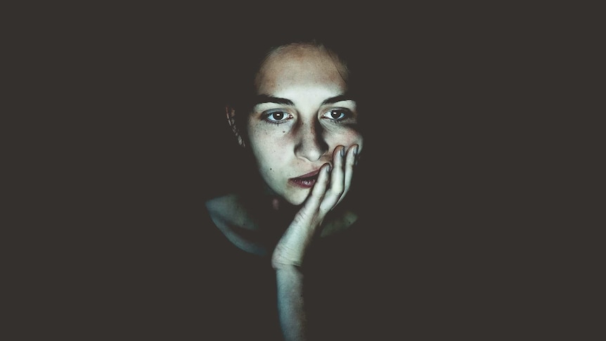 Woman's face, looking bored, surrounded by black background.