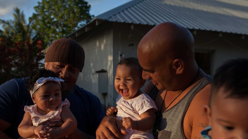 Christmas Island fathers hold up their babies as their partners watch on.