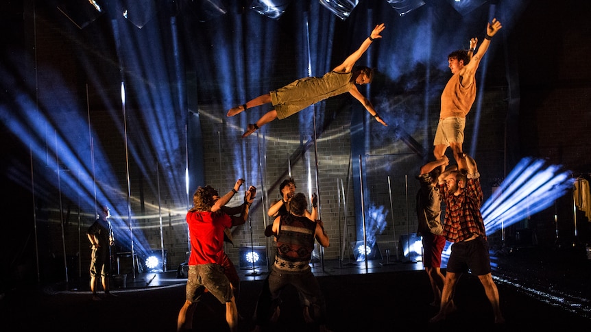 Acrobat Jascha Boyce flies through the air while fellow performers watch from below.