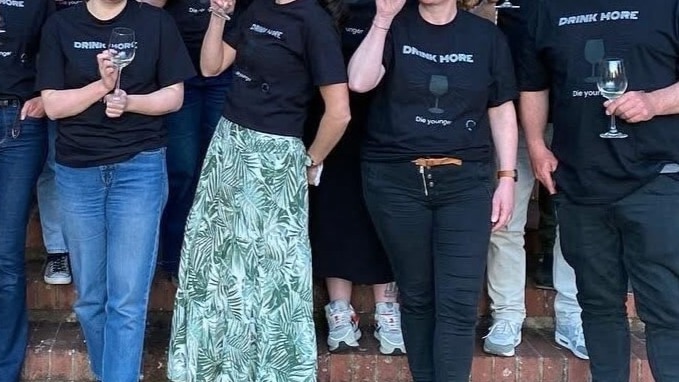 People standing in a group wearing T-shirts that say "drink more, die younger".