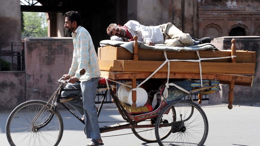 A man takes a nap on a bed being transported by cycle rickshaw in Amritsar, India