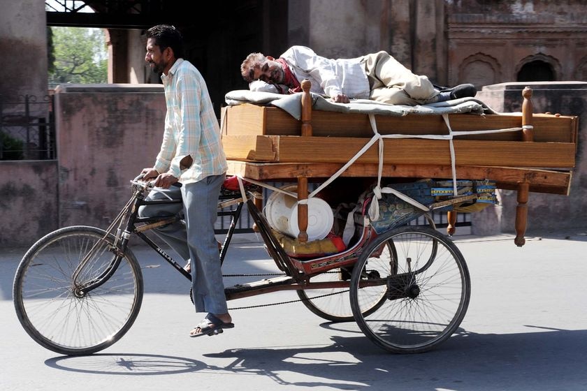 A man takes a nap on a bed being transported by cycle rickshaw in Amritsar, India