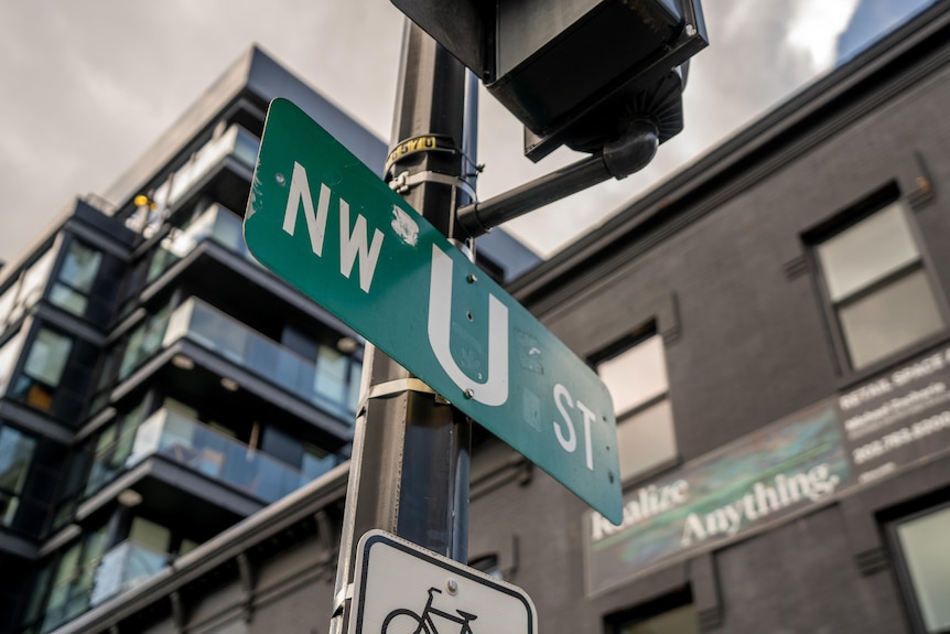 A street sign says 'NW U ST' under a traffic light. There are high rise apartments with balconies behind it.