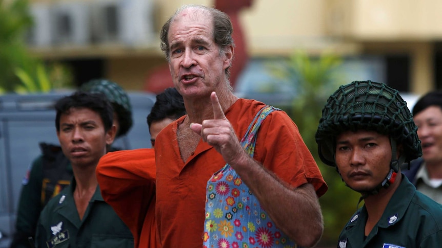 James Ricketson speaks and points towards the camera while surrounded by prison officials.