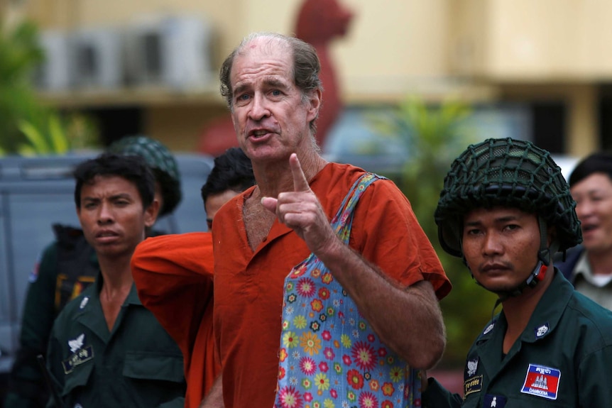 James Ricketson speaks and points towards the camera while surrounded by prison officials.