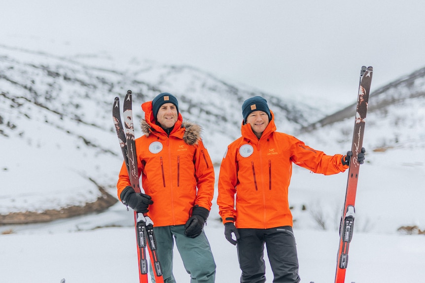 Two men stand in the snow with their skiis. 