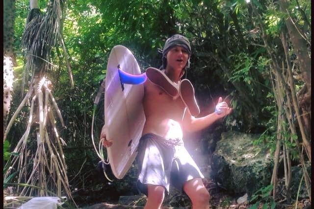 A man with a surfboard smiles while standing ona  path to the beach