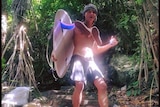 A man with a surfboard smiles while standing ona  path to the beach