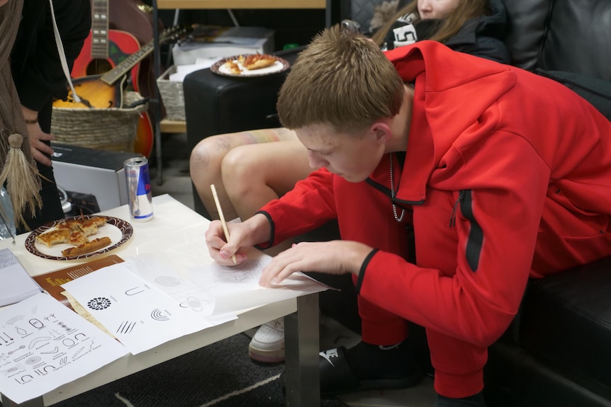 a man in a red tracksuit drawing at a table.