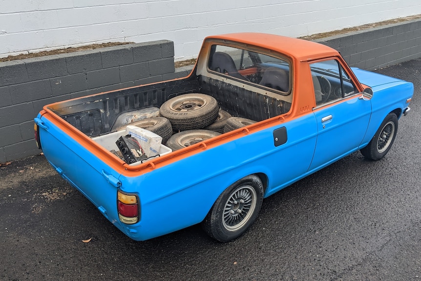A blue and orange two-door ute with tyres in the tray