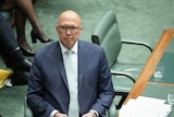 Peter Dutton wearing a suit sits at the desk in the House of Representatives. 