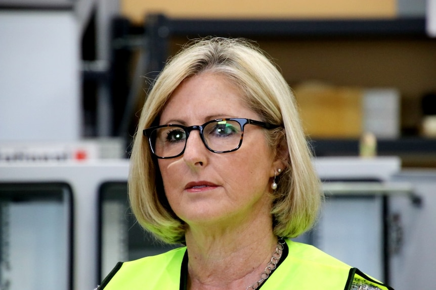 A close-up of a woman wearing black glasses and a high-vis vest.