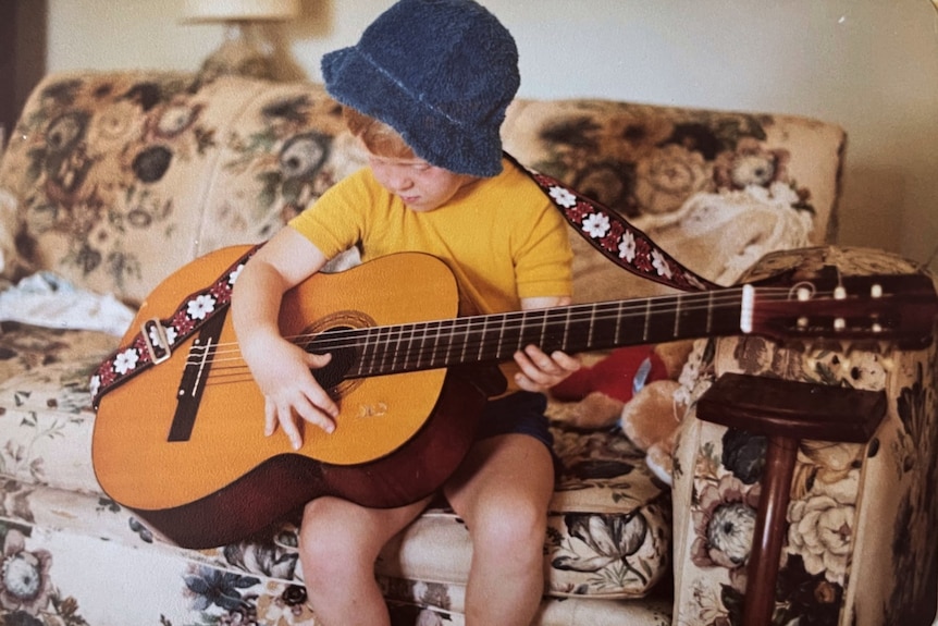 A young boy in a yellow t-shirt plays guitar.