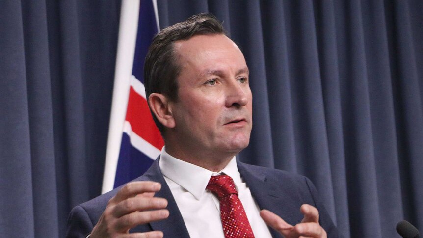 Mark McGowan in a suit standing at a lectern with a WA flag behind him