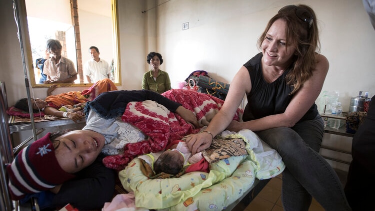 A woman sitting on a bed beside a woman with a newborn baby