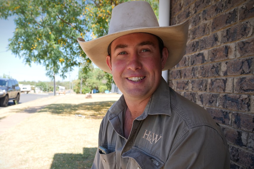 A man wearing a work shirt and hat smiles.