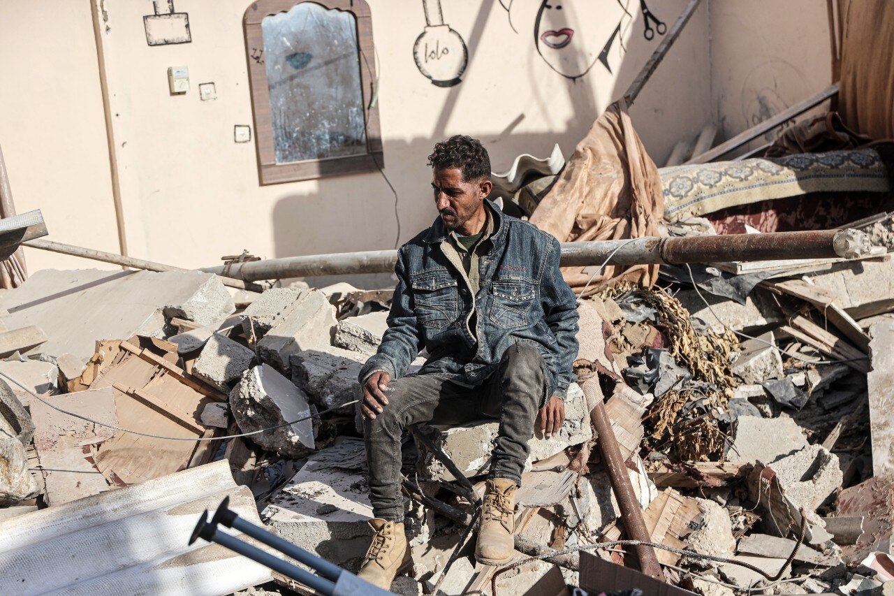 A man sitting on a pile of rubble, looking on.