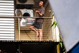 Man on the balcony of home emptying a dryer into a basket and feeling for rain.