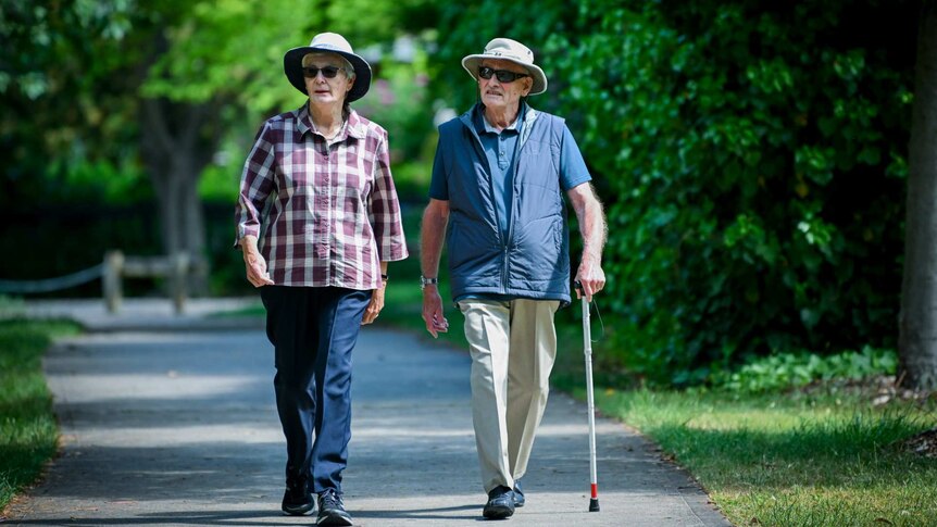 Two elderly walking people walking down the street.