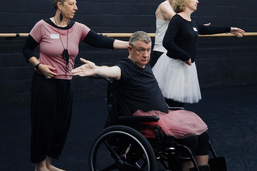 A man in a wheelchair with one arm out stretched wearing a pink tutu 
