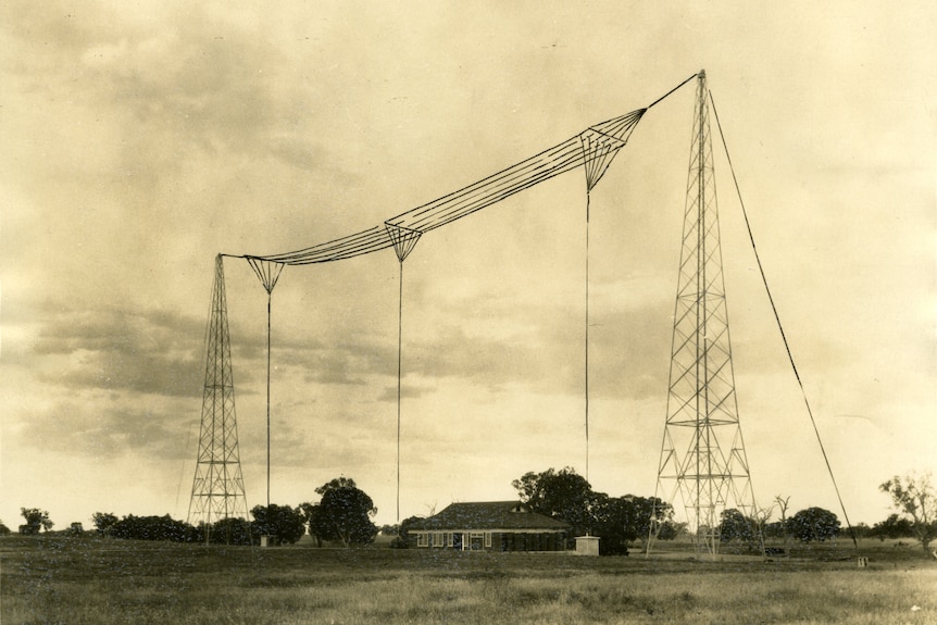 A sepia photo of a large radio transmitter overlooking a house.