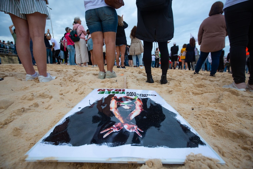 Faceless people line up with signs on the sand of Bondi Beach. 