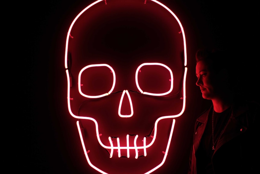 Julie McLaren stands next to a large pink skull in the dark
