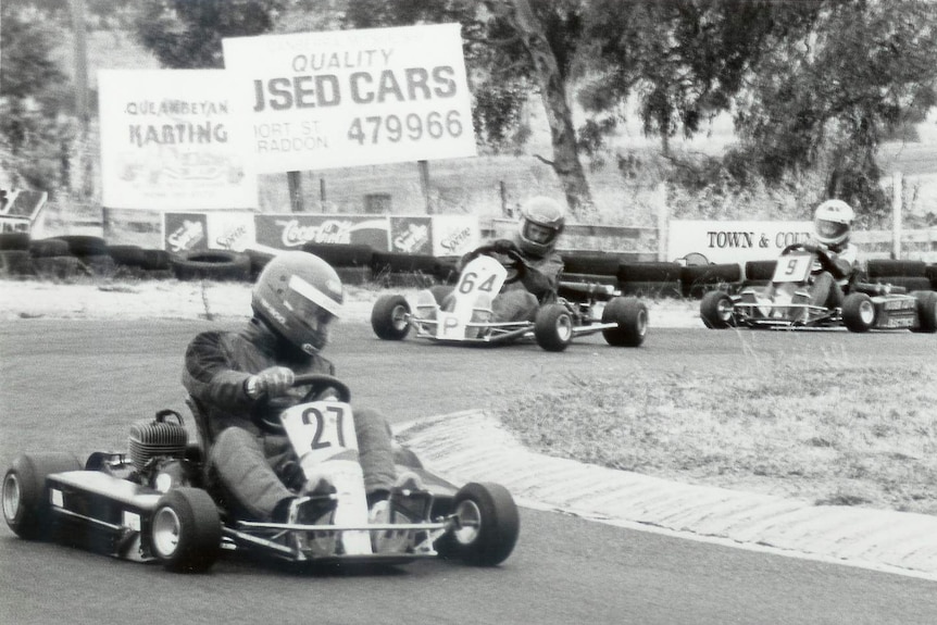 Mark Webber is trailed by two kart racers.