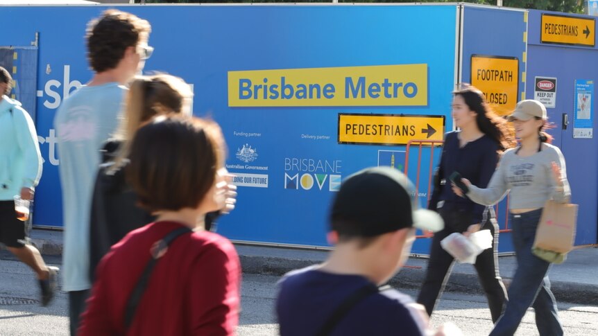 Pedestrians cross Adelaide Street near Brisbane Metro hoarding