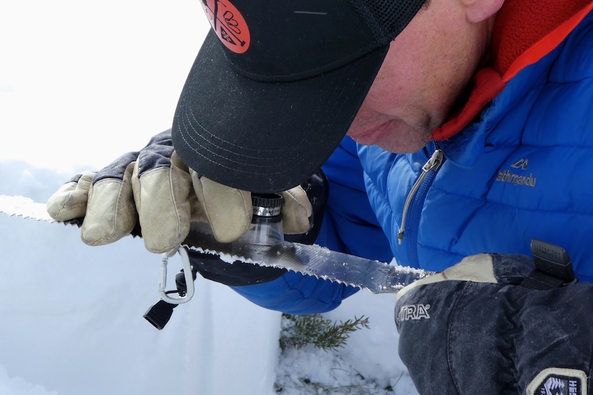 A man holds a magnifying glass to examine snow.