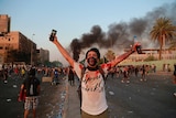 A protester with a white, blood-stained shirt stands in front of a huge crowd with his arms open in defiance at sunset.