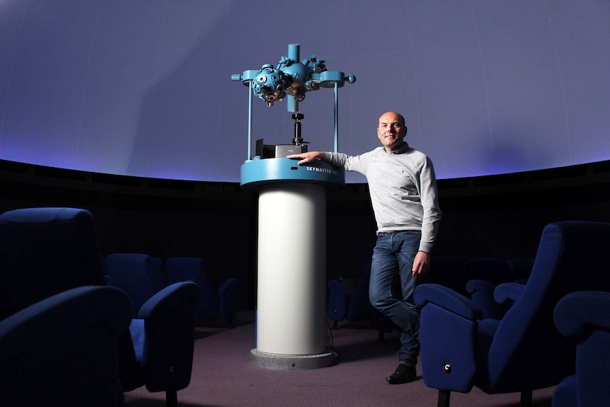 Stuart Creal stands inside the planetarium with his arm on the projector.