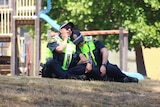 Two police officers sitting on the ground lean on each other.