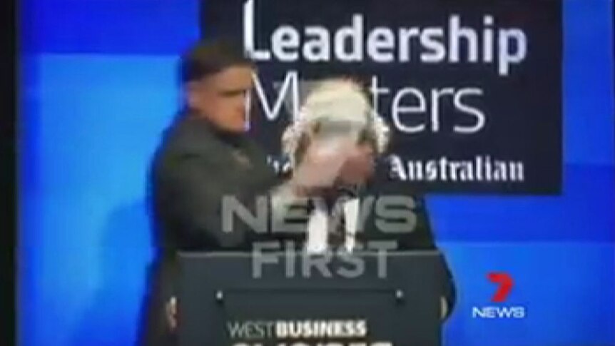 A man hits Qantas CEO Alan Joyce in the face with a cream pie after walking up behind him on stage.