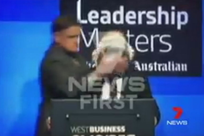 A man hits Qantas CEO Alan Joyce in the face with a cream pie after walking up behind him on stage.