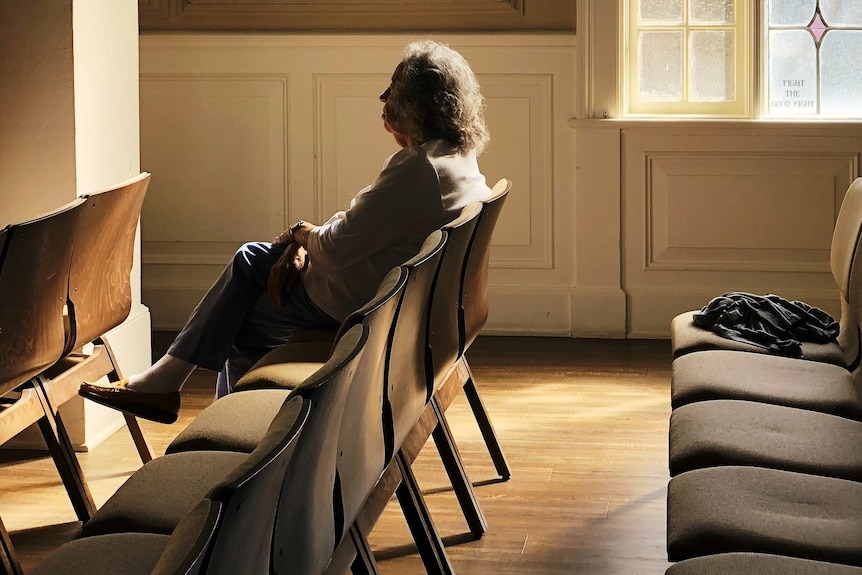 Elderly lady sitting alone, surrounded by rows of chairs.