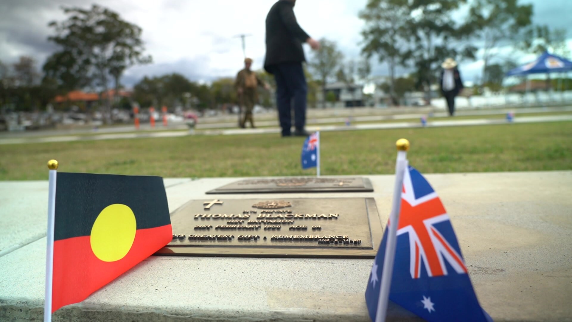 a close-up shot taken from ground level of a memorial plaque in a cemetery. the aboriginal and australian flags are next to it