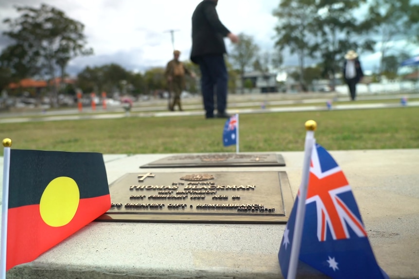 a close-up shot taken from ground level of a memorial plaque in a cemetery. the aboriginal and australian flags are next to it