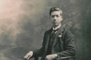 A historic photo in black in white of a man sitting on a chair.