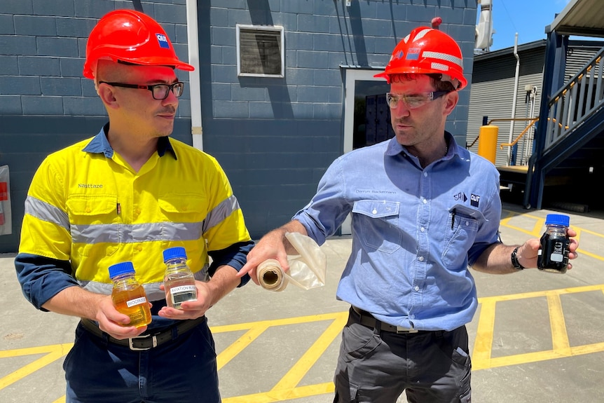 Two men in hi-vis and hard hats hold bottles of fuel and bioplastics. 